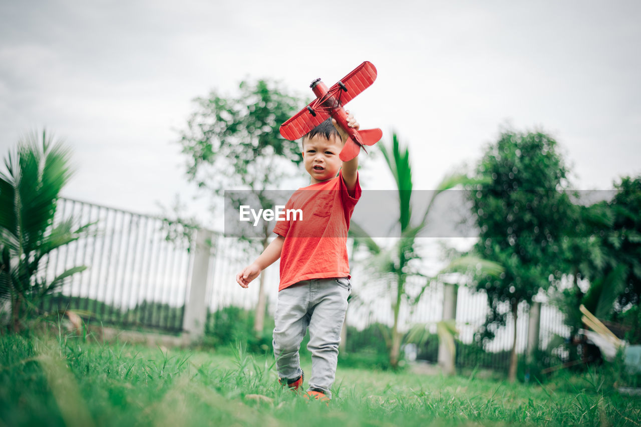 Boy with toy airplane on field against sky