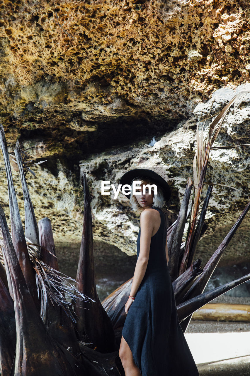 Side view portrait of young woman on driftwood against rock formation