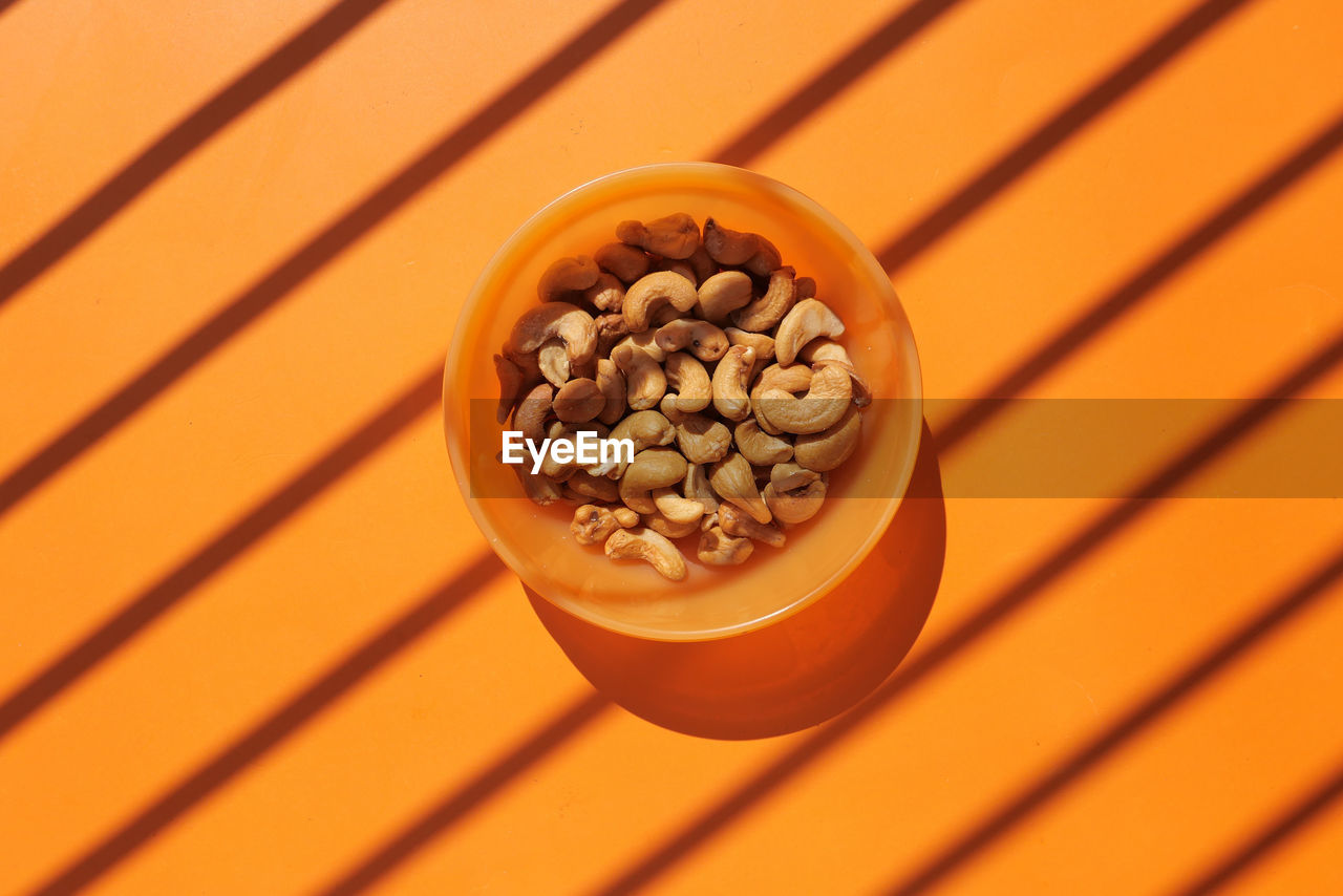 Top view of cashew nut in a bowl on orange background