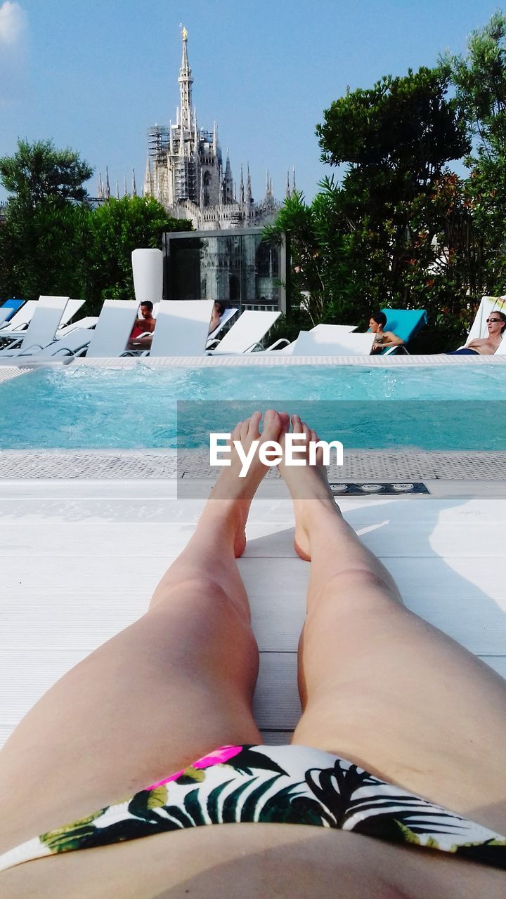 Low section of woman resting on lounge chair at poolside against duomo di milano