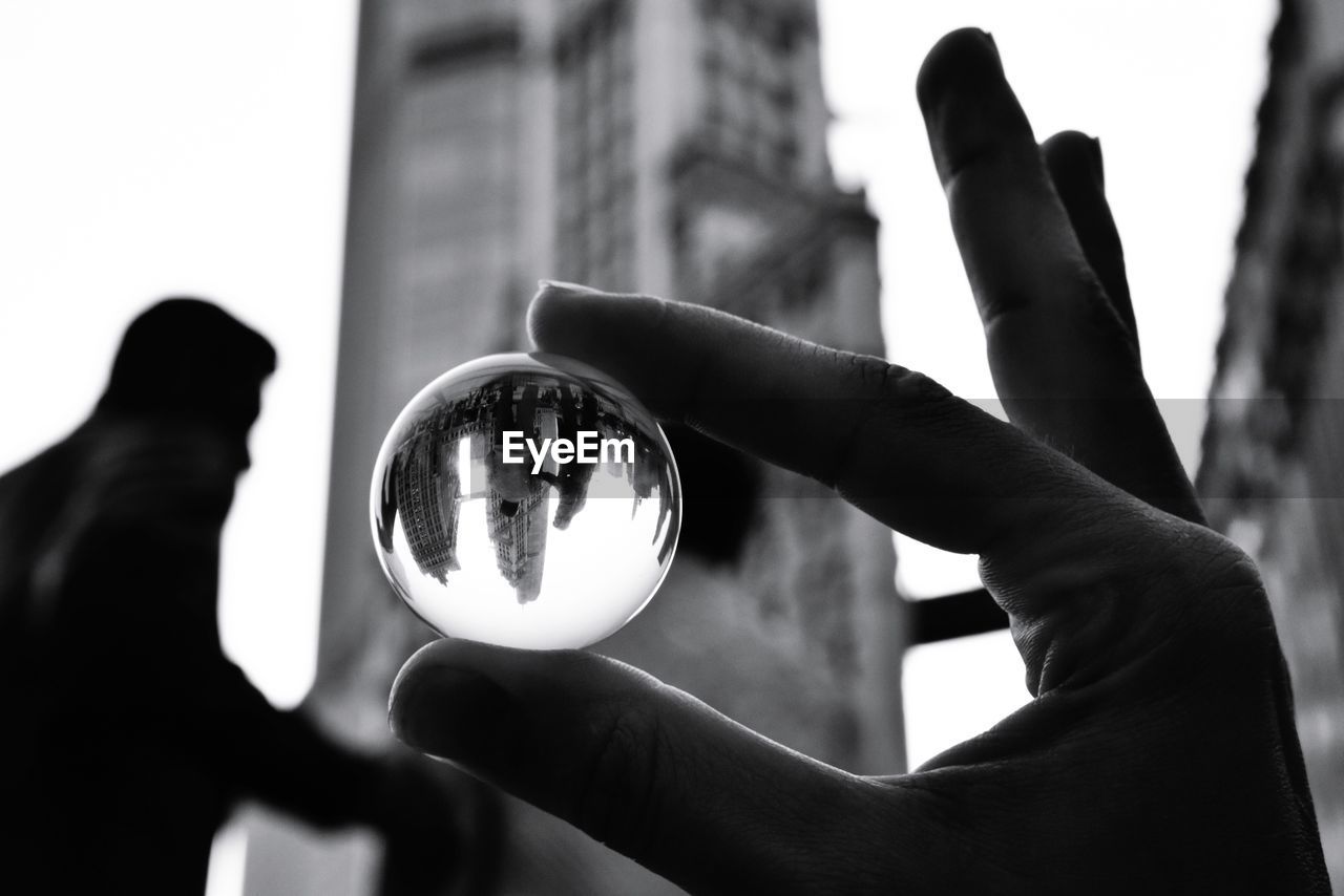 CLOSE-UP OF HAND HOLDING CRYSTAL BALL WITH BLURRED BACKGROUND