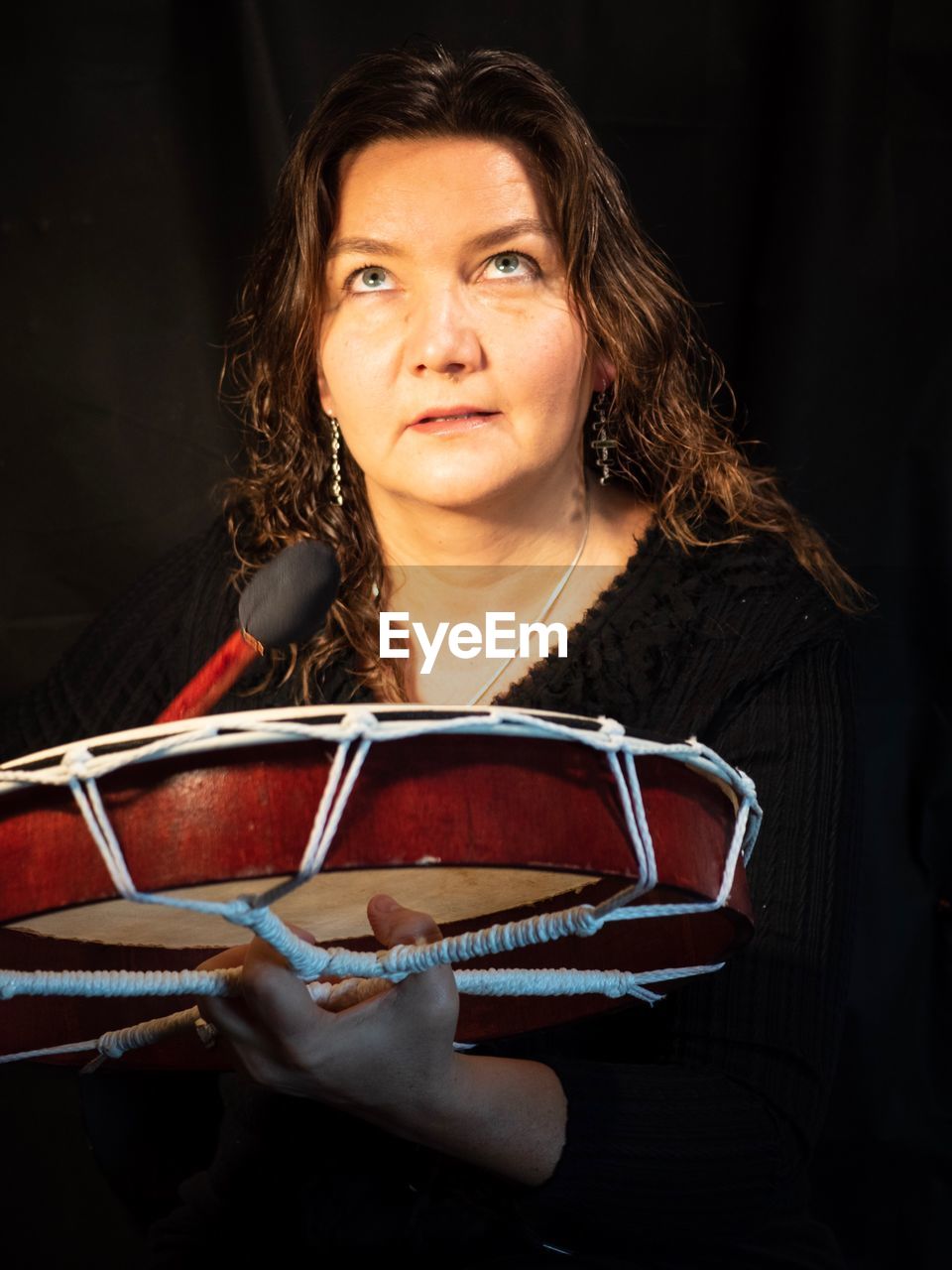 Mature woman looking up while holding musical equipment against black background