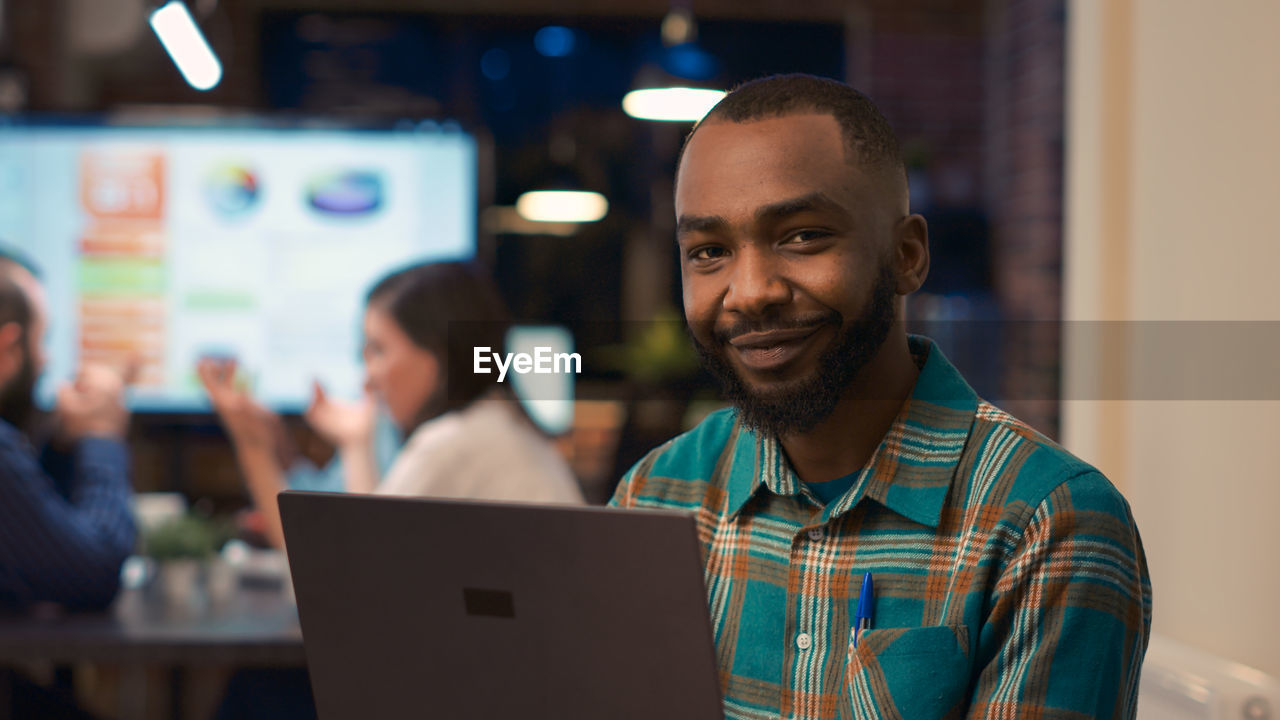 portrait of man using laptop while standing in office