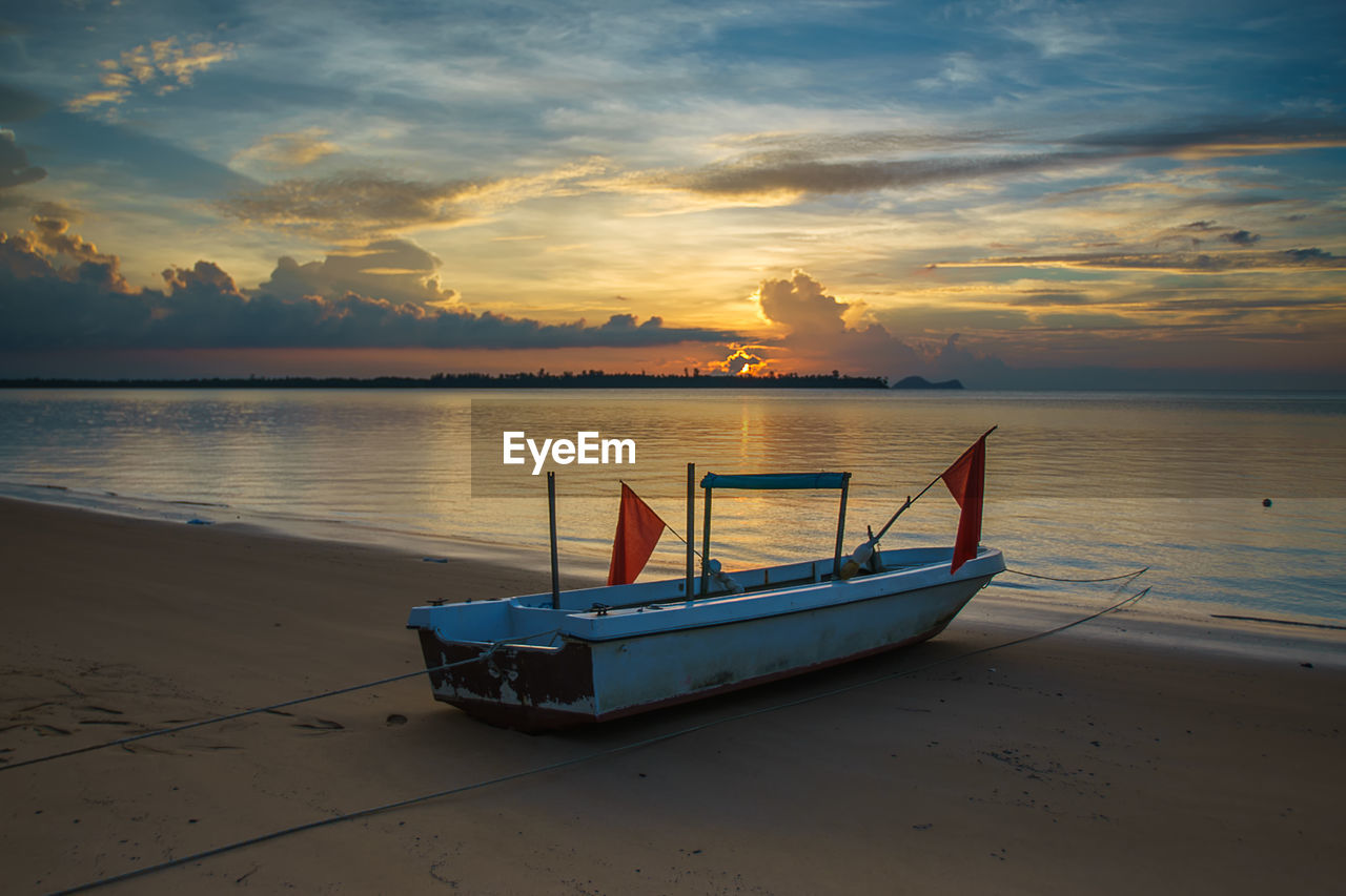 Boat moored at beach against sky during sunset