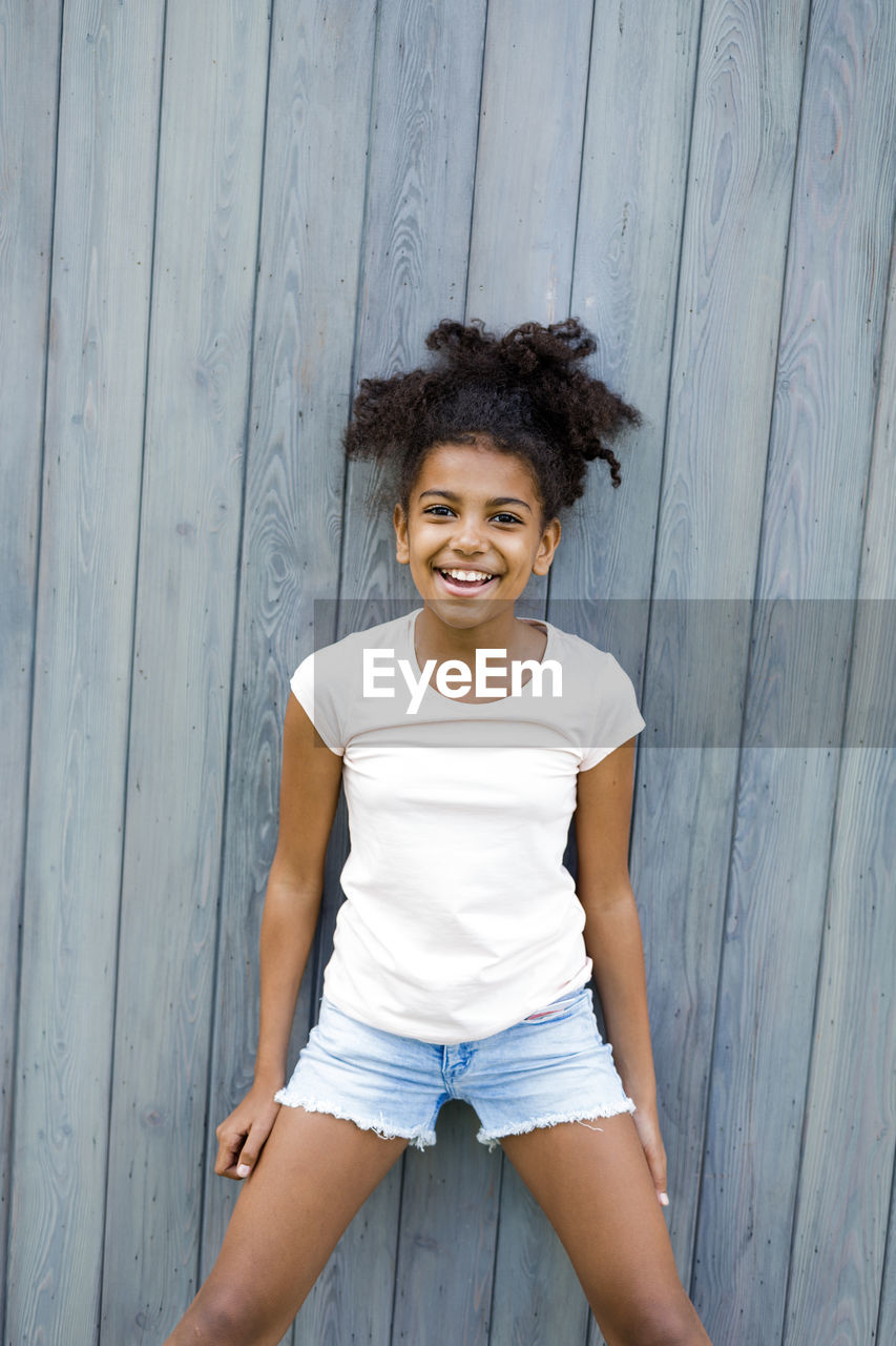 Portrait of happy girl standing by wooden wall