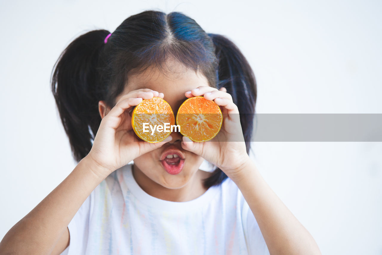 Close-up of girl holding orange slices against white background