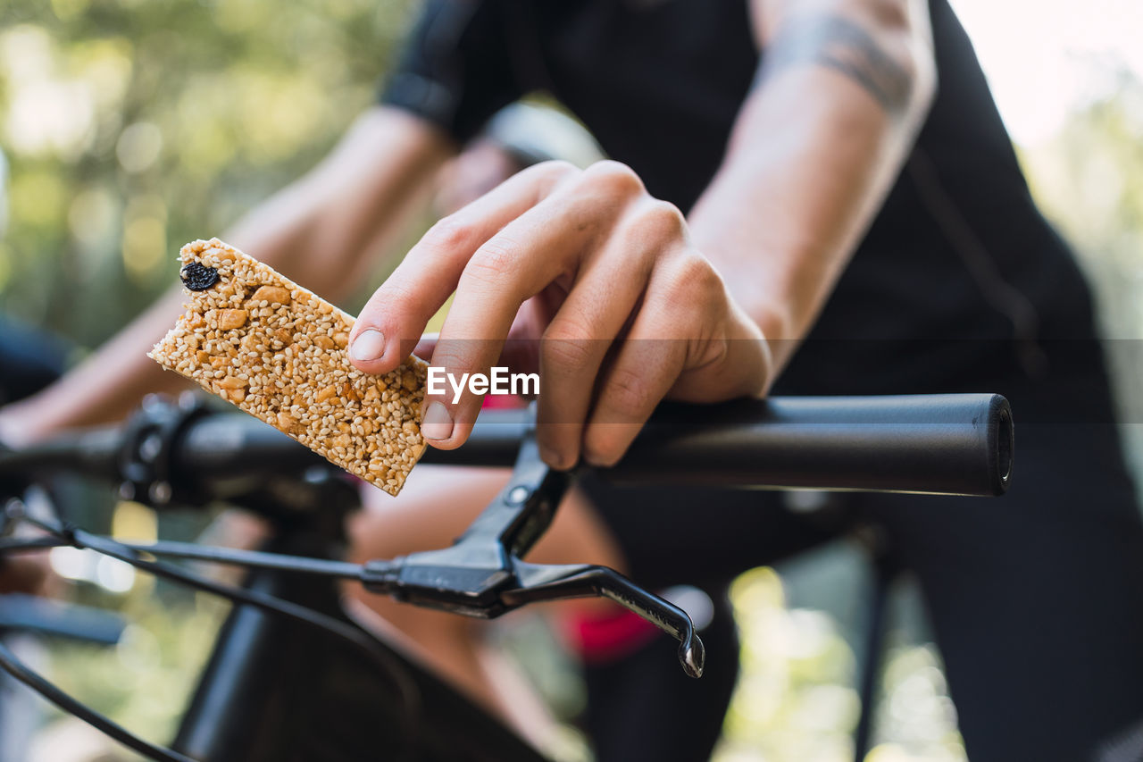 From below of sportspeople in helmets with cereal bars riding bicycles during workout in daylight