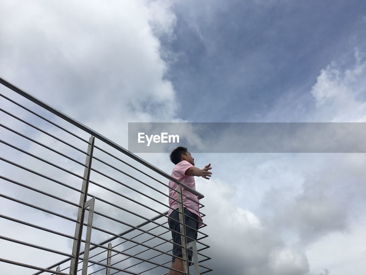 Low angle view of carefree man standing on balcony against cloudy sky