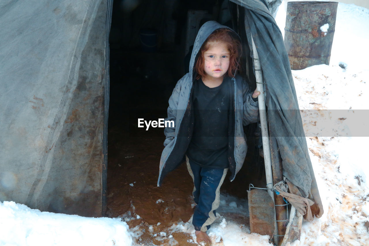 A syrian refugee child at the door of his snow covered tent