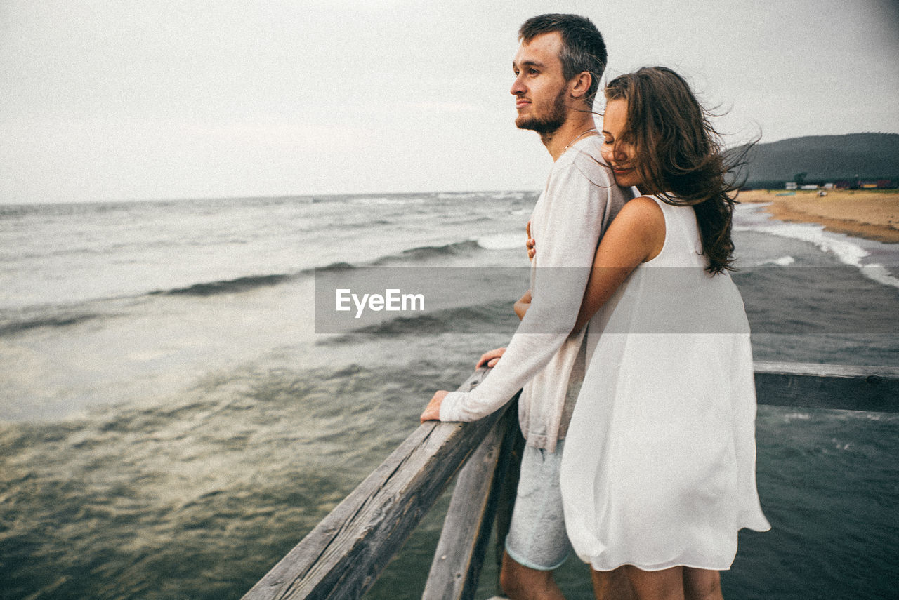 FRIENDS STANDING ON BEACH AGAINST SKY