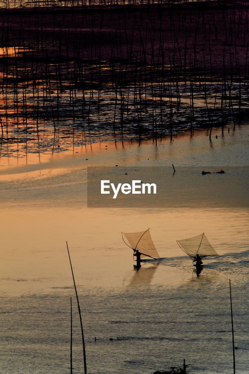 Silhouette fishing net on sea against sky during sunset