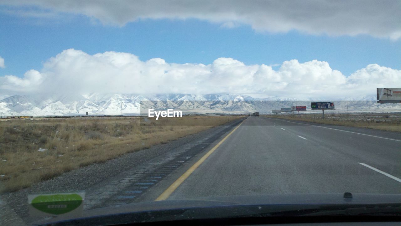 Road leading towards snowcapped mountains seen through car windshield