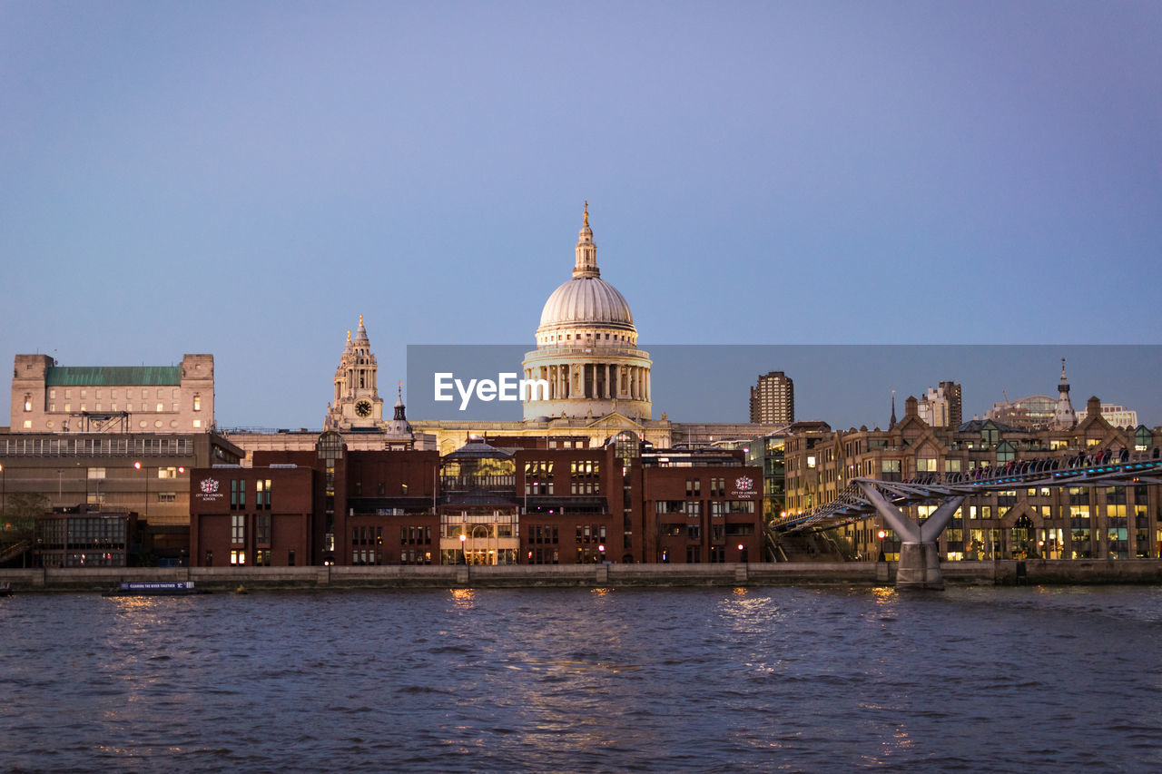 Church amidst city by river against clear sky