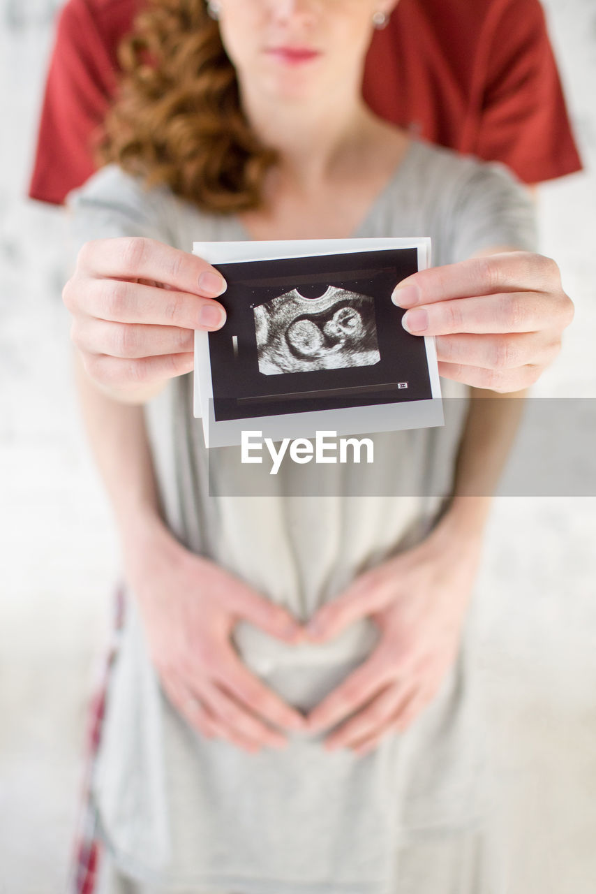 Midsection of pregnant woman holding instant print transfer while standing with man