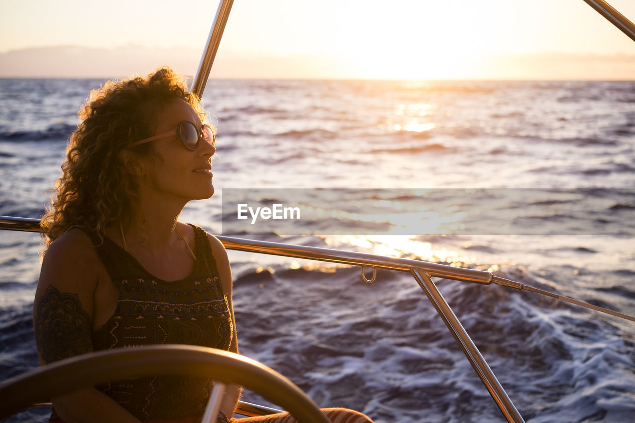 WOMAN SITTING BY BOAT AGAINST SEA