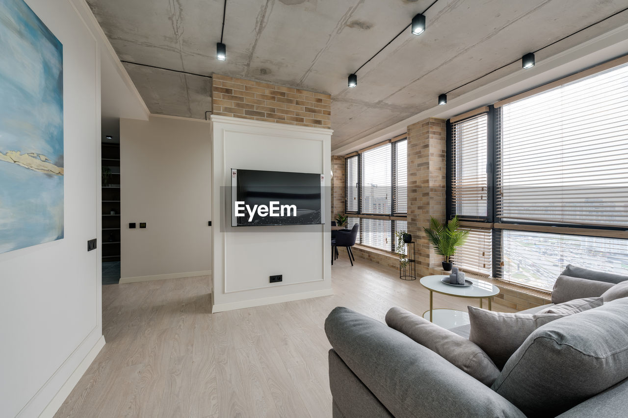 Interior in a modern style and a view of the tv and part of the kitchen near the large windows 