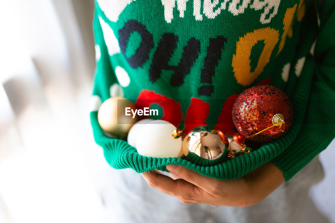 Midsection of woman carrying christmas ornament in sweater