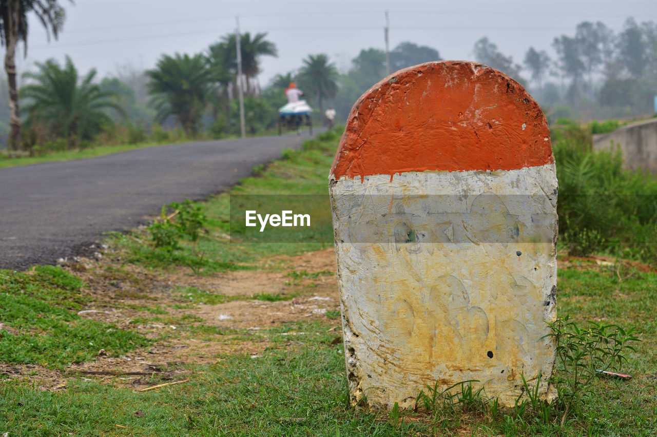 Close-up of blank milestone  beside the road amidst trees on field.