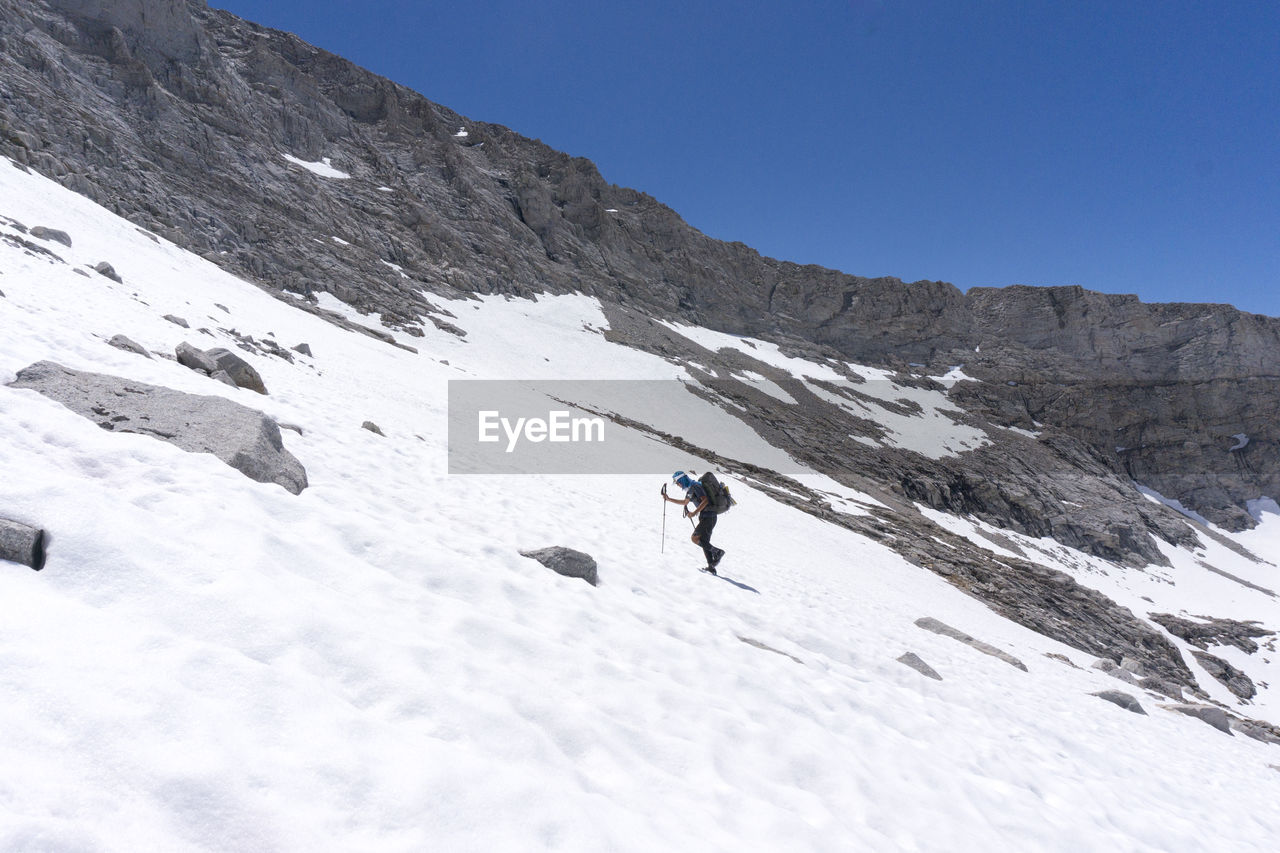 Side view of man walking on snowcapped mountain against clear sky