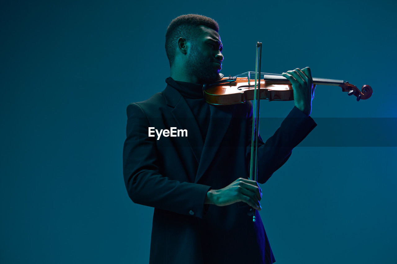 low angle view of man playing violin against blue background