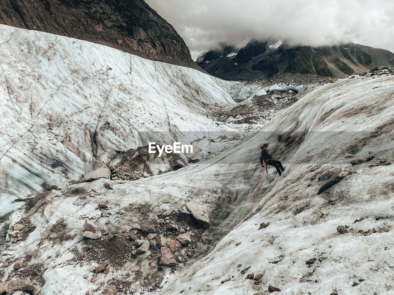 Landscape shot of climber rappelling on glacier under cloudy sky