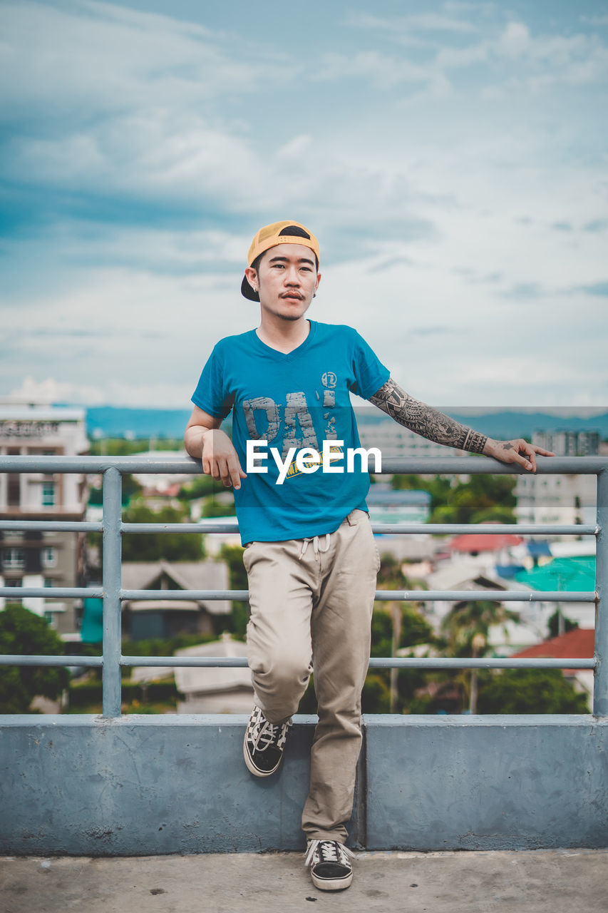 Portrait of young man standing against railing in city