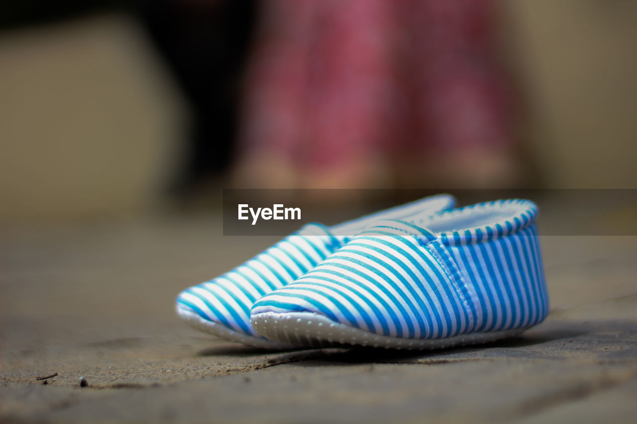 Close-up of baby shoes on the road where parents is standing in background