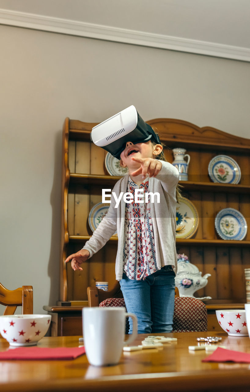 Smiling girl wearing virtual reality headset while pointing at table