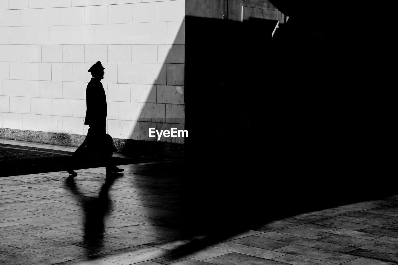 SILHOUETTE MAN WALKING ON FOOTPATH AGAINST STREET