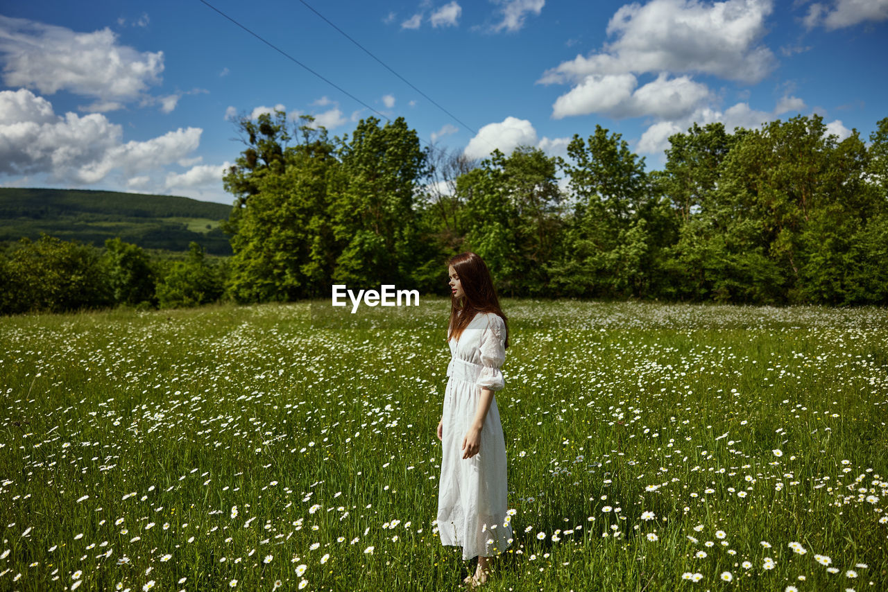 young woman standing on field against sky