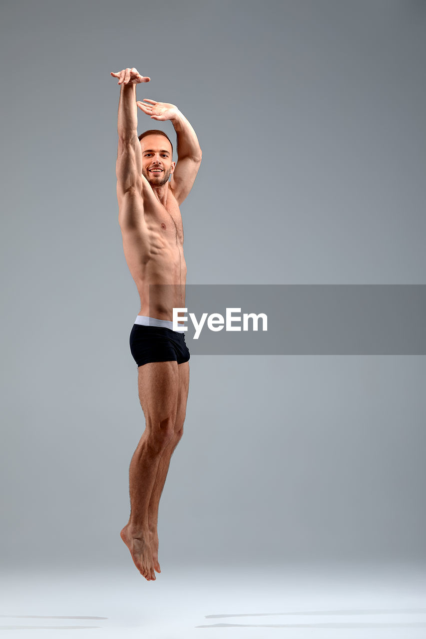 full length of young woman with arms raised standing against white background