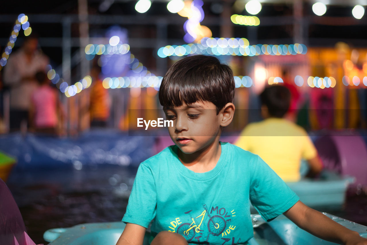 Cute boy looking down against illuminated lighting equipment at night