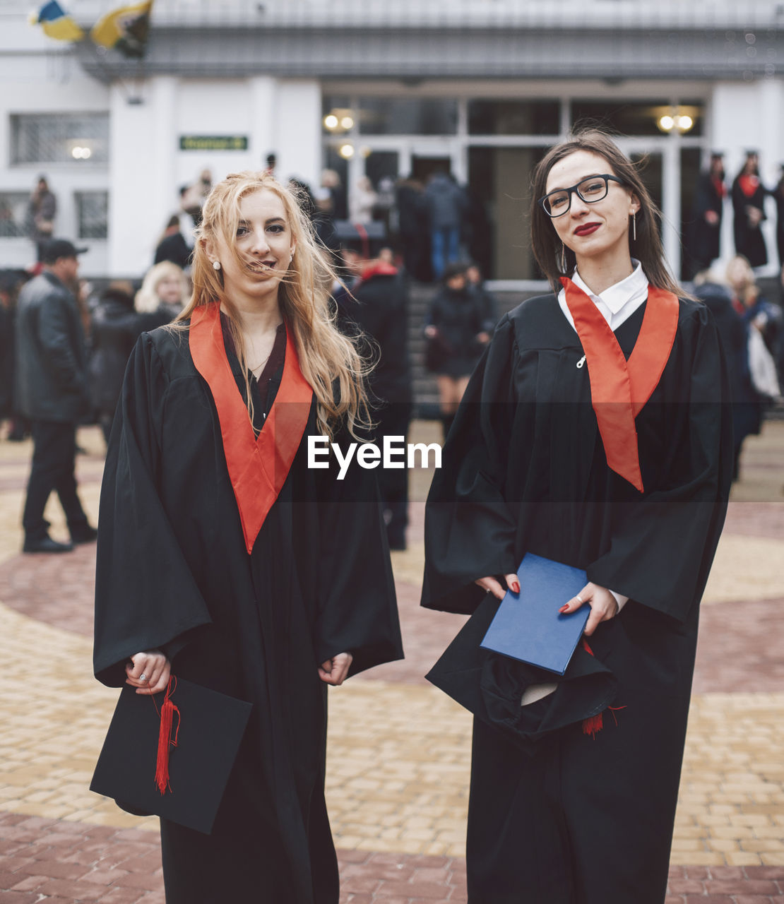 Portrait of happy female students wearing graduation gowns while standing against building