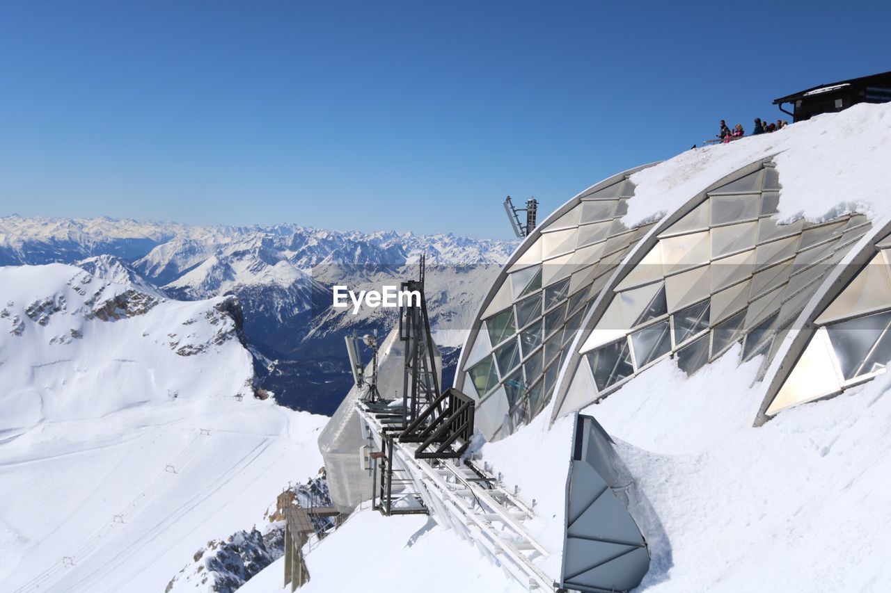 Glass dome by snowcapped mountain against blue sky