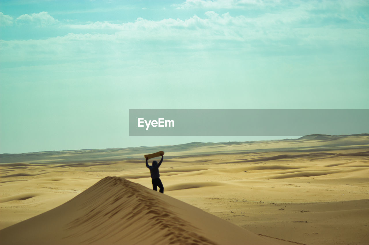 rear view of man walking on sand at desert against sky