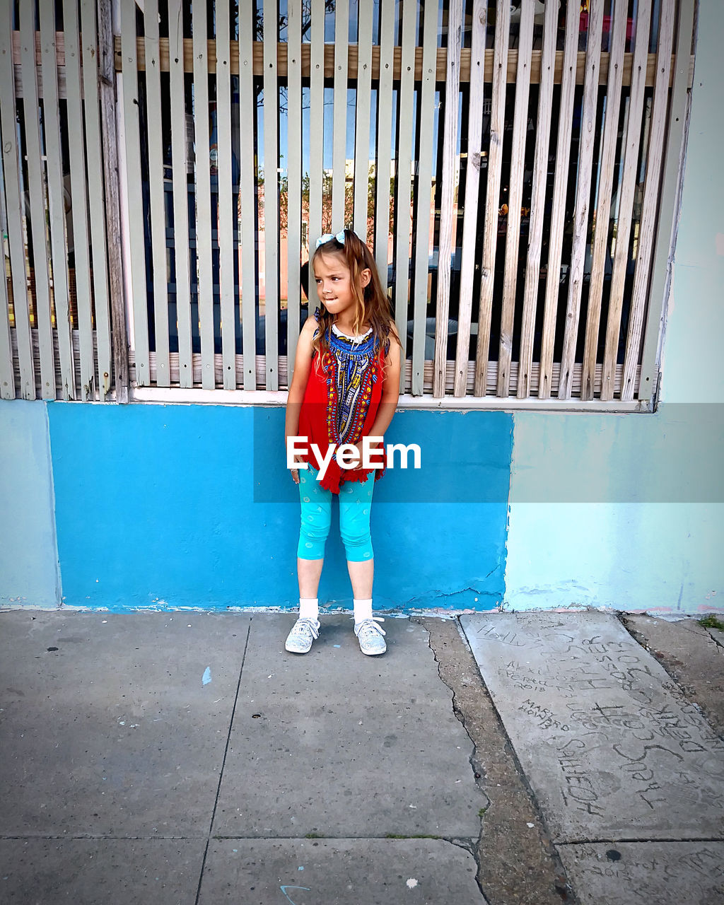 FULL LENGTH PORTRAIT OF SMILING GIRL STANDING AGAINST BLUE WALL