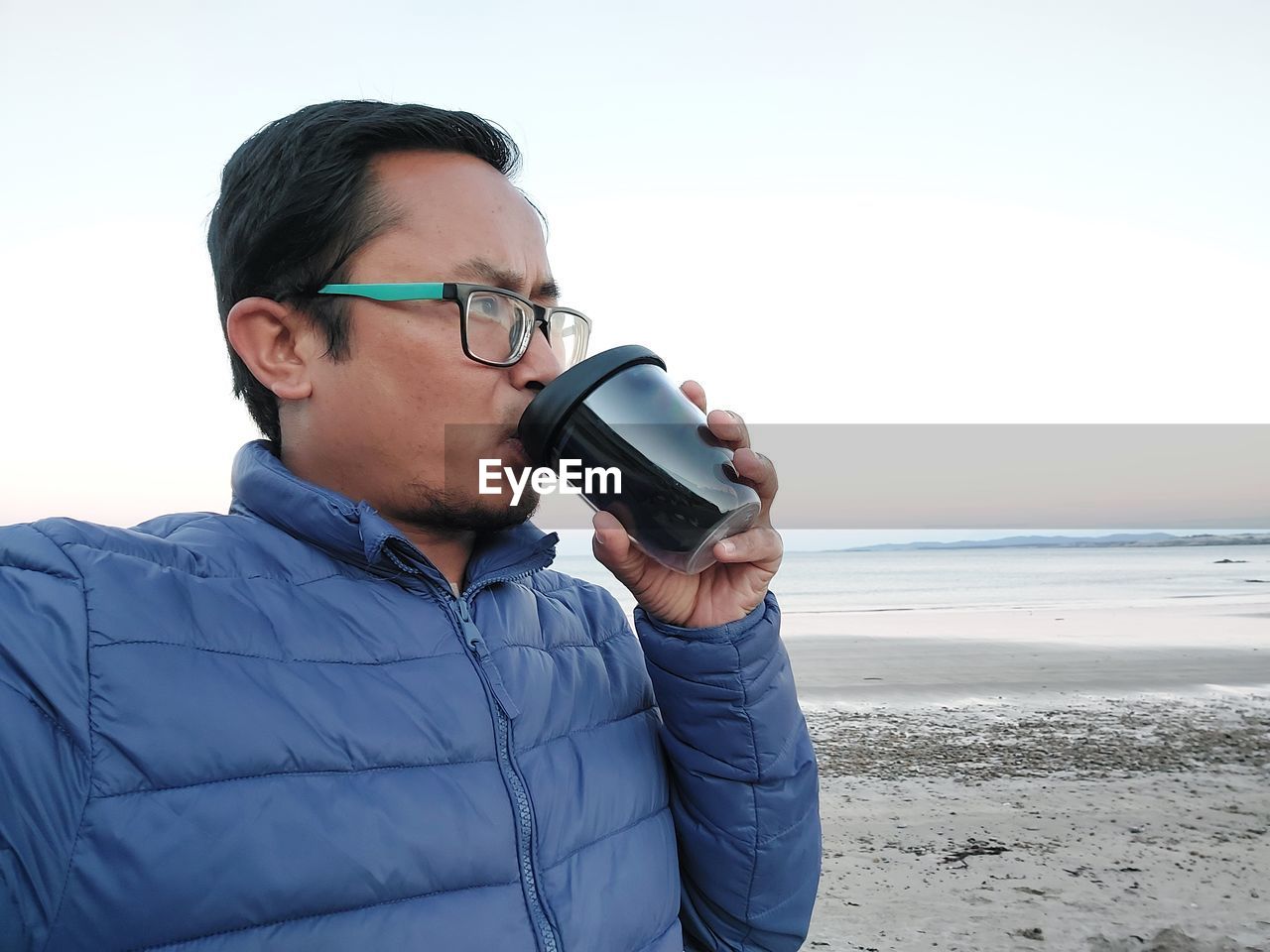 Side view of young woman drinking water while standing at beach