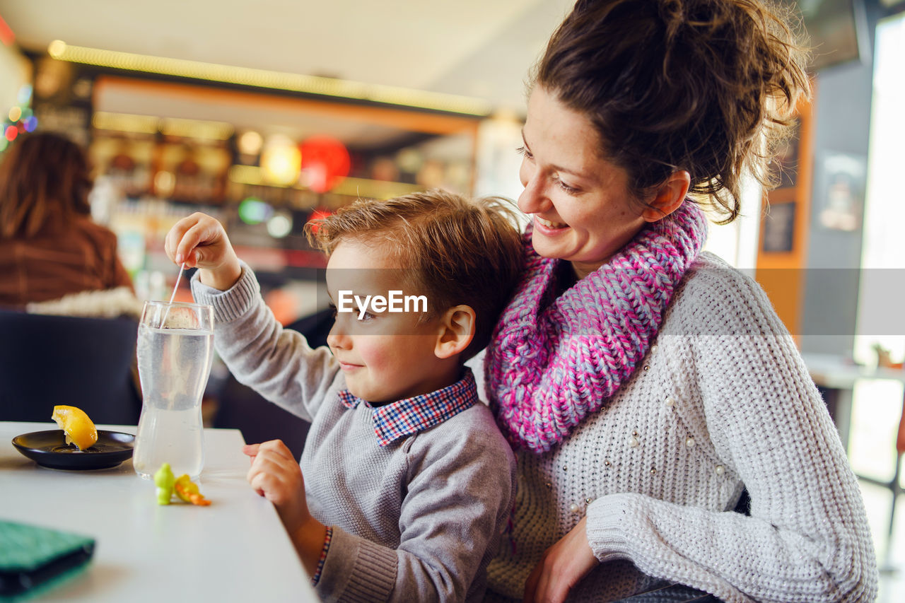 Smiling woman sitting with son at table in restaurant