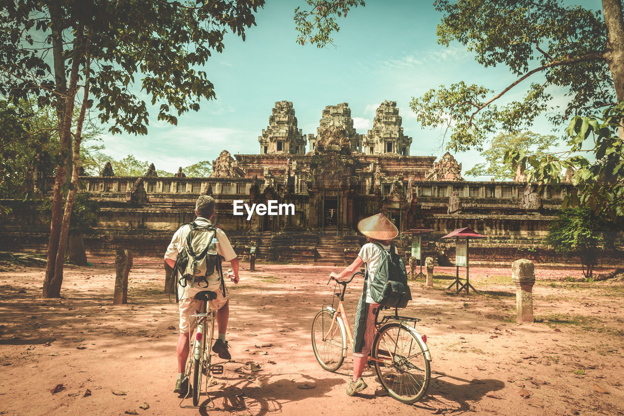 Rear view of people with bicycles in front of temple