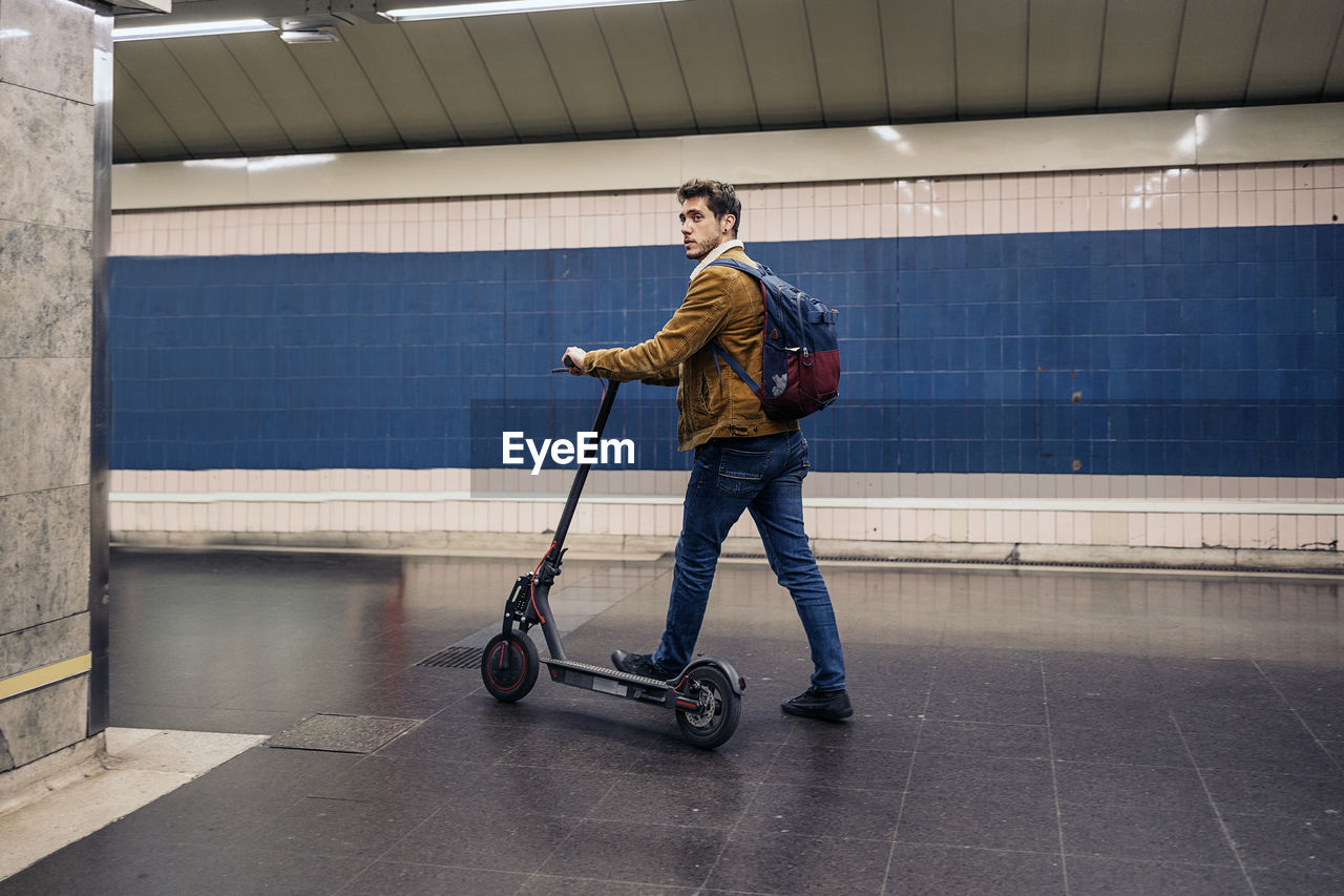 Full length of man with electric push scooter standing on subway station