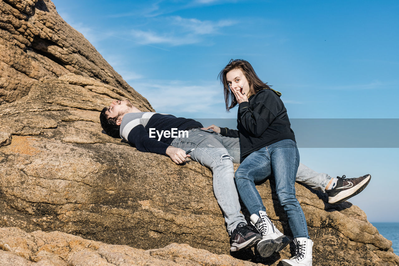 rock, one person, adult, sky, nature, full length, leisure activity, activity, young adult, casual clothing, footwear, mountain, adventure, lifestyles, sports, relaxation, land, day, women, extreme sports, outdoors, blue, sitting, communication, looking, emotion, jeans, men, cloud, clothing, sunlight, recreation, low angle view