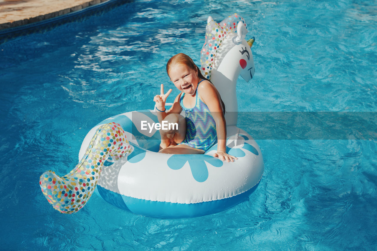 Smiling caucasian girl lying on inflatable ring unicorn. kid child having fun in swimming pool