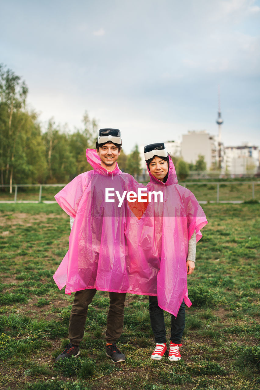 Happy young couple wearing raincoat and virtual reality simulator at park