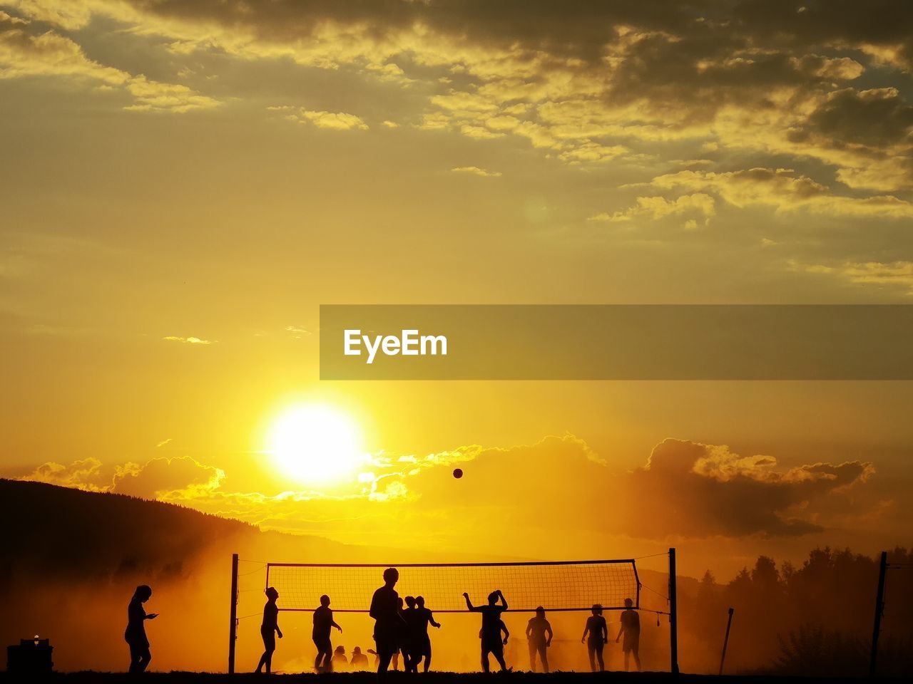 Silhouette of people playing volleyball against sky during sunset