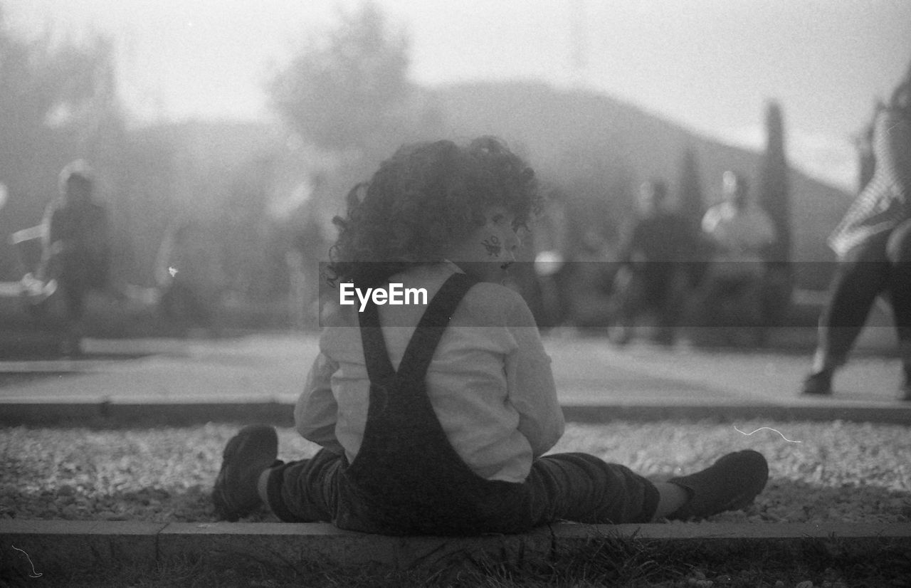 REAR VIEW OF BOY SITTING ON STREET