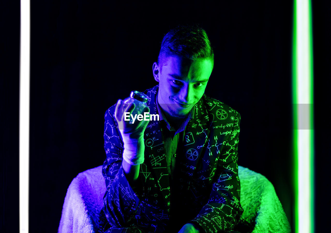 Young man looking away while sitting against black background