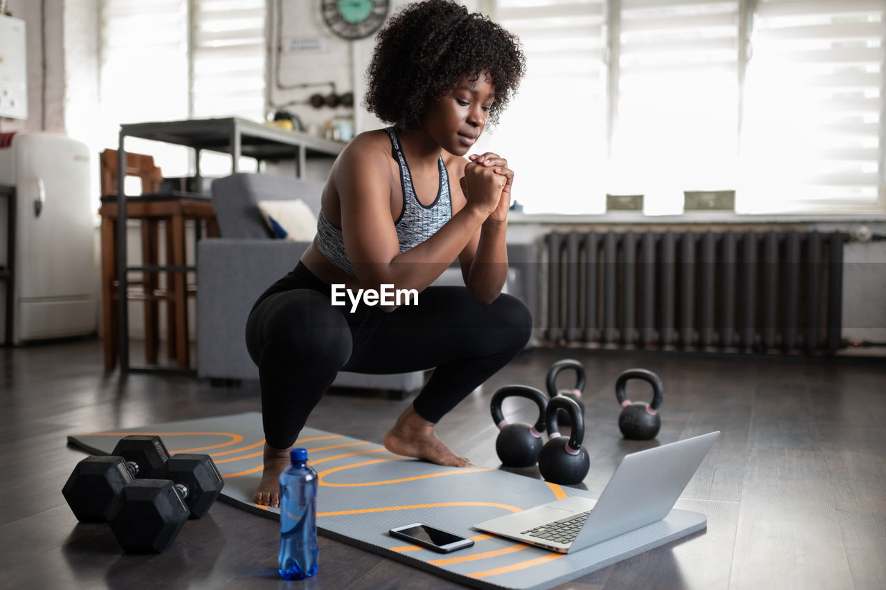 African american sportswoman squatting during online workout