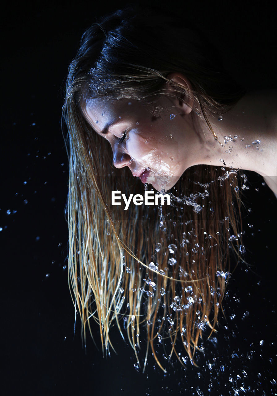 Side view of woman with water on face against black background