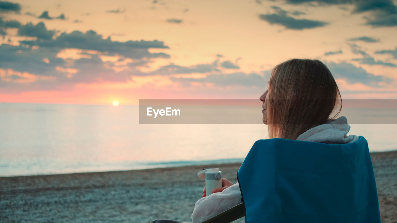 REAR VIEW OF WOMAN ON BEACH AGAINST SKY DURING SUNSET