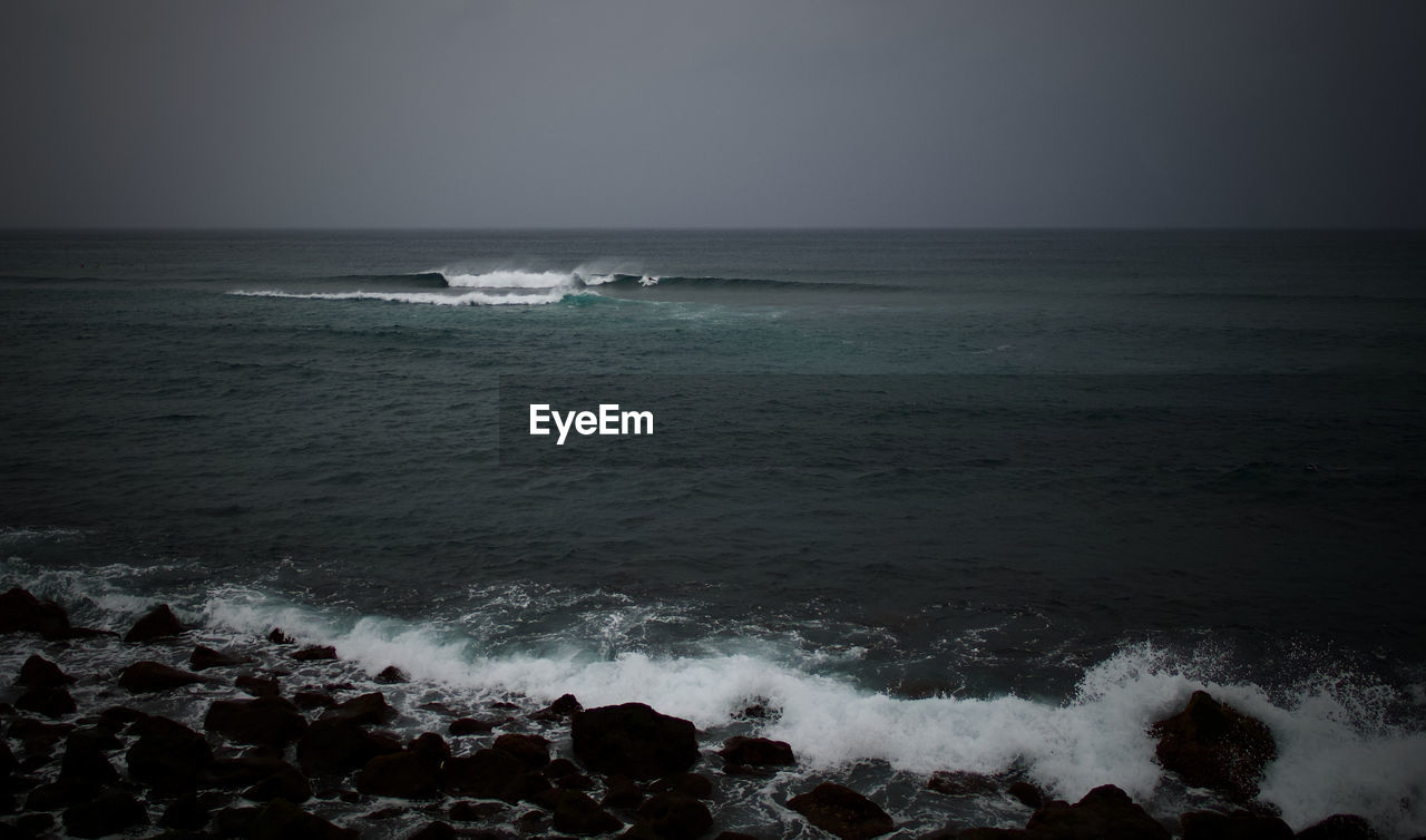 sea, water, horizon, wave, beach, land, ocean, wind wave, motion, sky, horizon over water, beauty in nature, scenics - nature, body of water, nature, rock, shore, coast, black and white, surfing, sports, water sports, monochrome, monochrome photography, tranquility, darkness, outdoors, dusk, seascape, tranquil scene, environment, travel destinations, idyllic, coastline, cloud